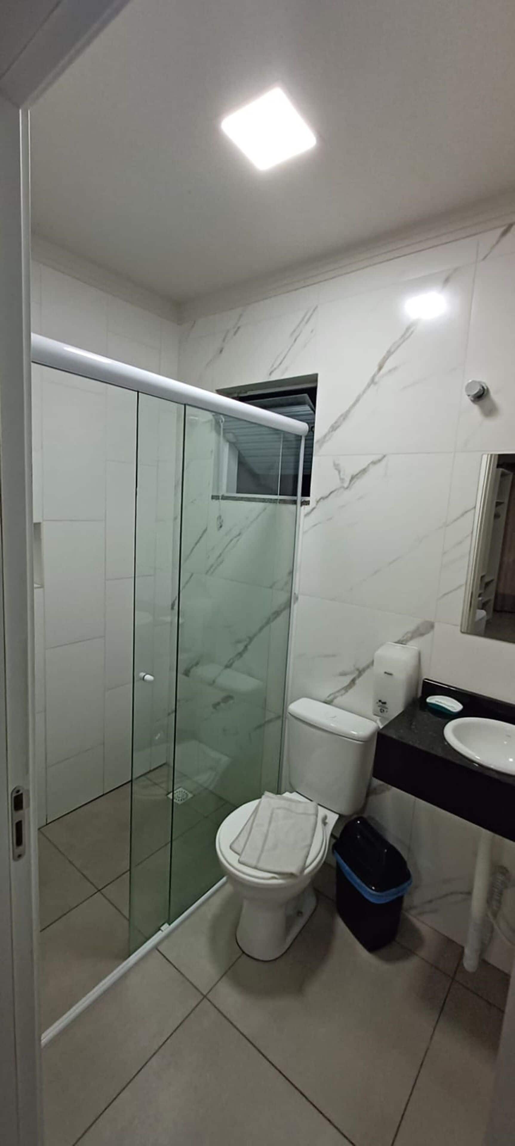Une salle de bain moderne avec une douche à parois de verre, des toilettes blanches, une poubelle noire et un plan de toilette noir avec un lavabo blanc.