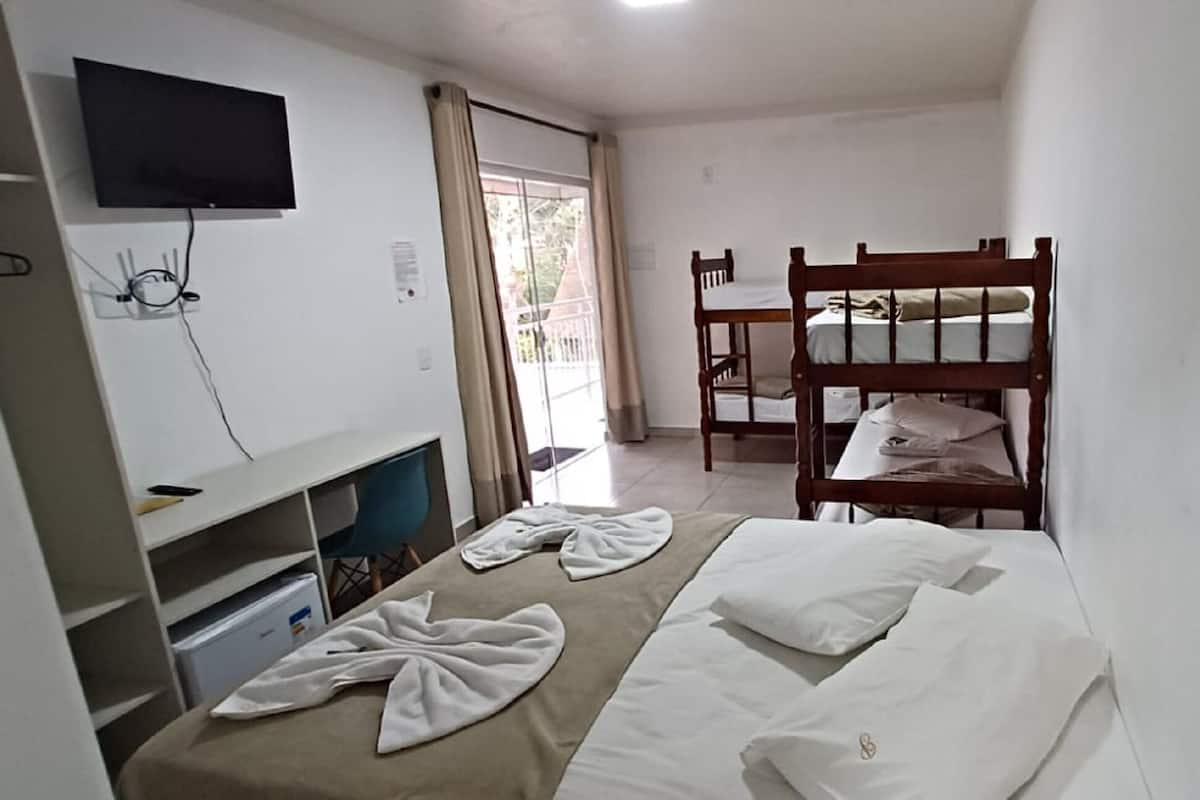 A bedroom with bunk beds, a TV mounted on the wall, a desk with a chair, and a window with curtains.