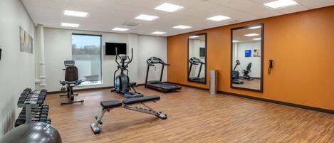 A gym with exercise equipment, a mirror, and a window.