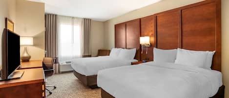 A hotel room with two beds, a desk with a TV, a lamp, and a view of the outdoors.