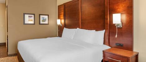 A hotel room with a large bed, wooden headboard, bedside lamps, and a small wooden nightstand.