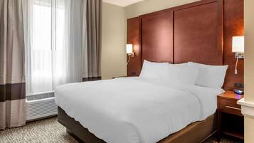 A hotel room with a large bed, a wooden headboard, a bedside table with a lamp, and a window with curtains.