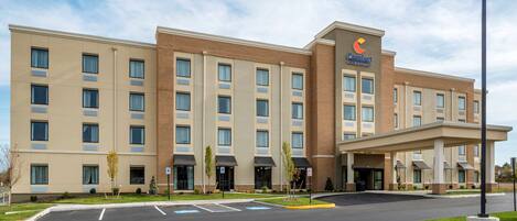A Comfort Inn hotel with a modern design, featuring a central entrance, multiple floors, and a parking lot.