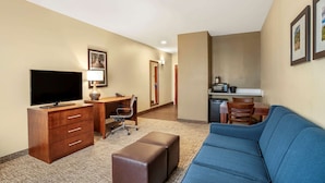 Ein Hotelzimmer mit Fernseher, Schreibtisch, Stuhl, Sofa und Küchenzeile.