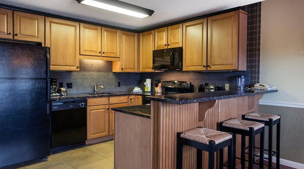 A kitchen with wooden cabinets, a black refrigerator, a microwave, and a bar area with stools.