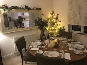 A dining area with a round table set for four, surrounded by chairs. A small Christmas tree with lights is placed in the center. - Cozy Nook Boutique Cottage (Oakham)