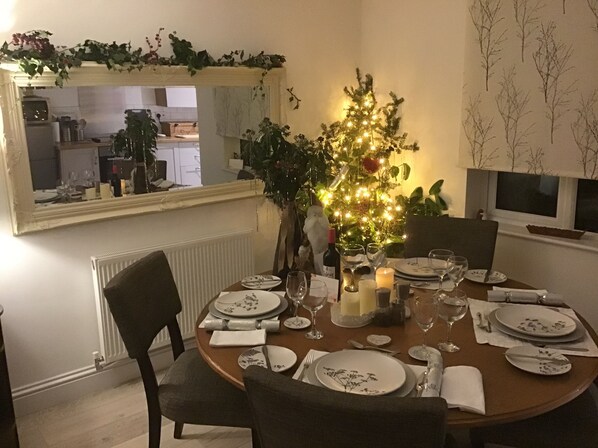 Un comedor con una mesa redonda dispuesta para cuatro personas, rodeada de sillas. Un pequeño árbol de Navidad con luces está colocado en el centro.