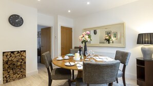 Un coin repas avec une table ronde dressée pour quatre personnes, des chaises, une horloge au mur, un miroir et un vase rempli de fleurs.