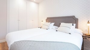 Un lit bien fait, avec une couvre-lit à motifs, une tête de lit ornée d’éléments décoratifs et une table de chevet avec une lampe.
