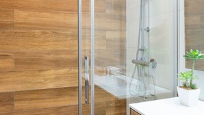 Une salle de bain moderne avec une douche à parois de verre, un plancher en bois et un lavabo blanc.
