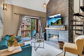 Una sala de estar moderna con chimenea, un televisor montado encima y un balcón con mobiliario exterior.
