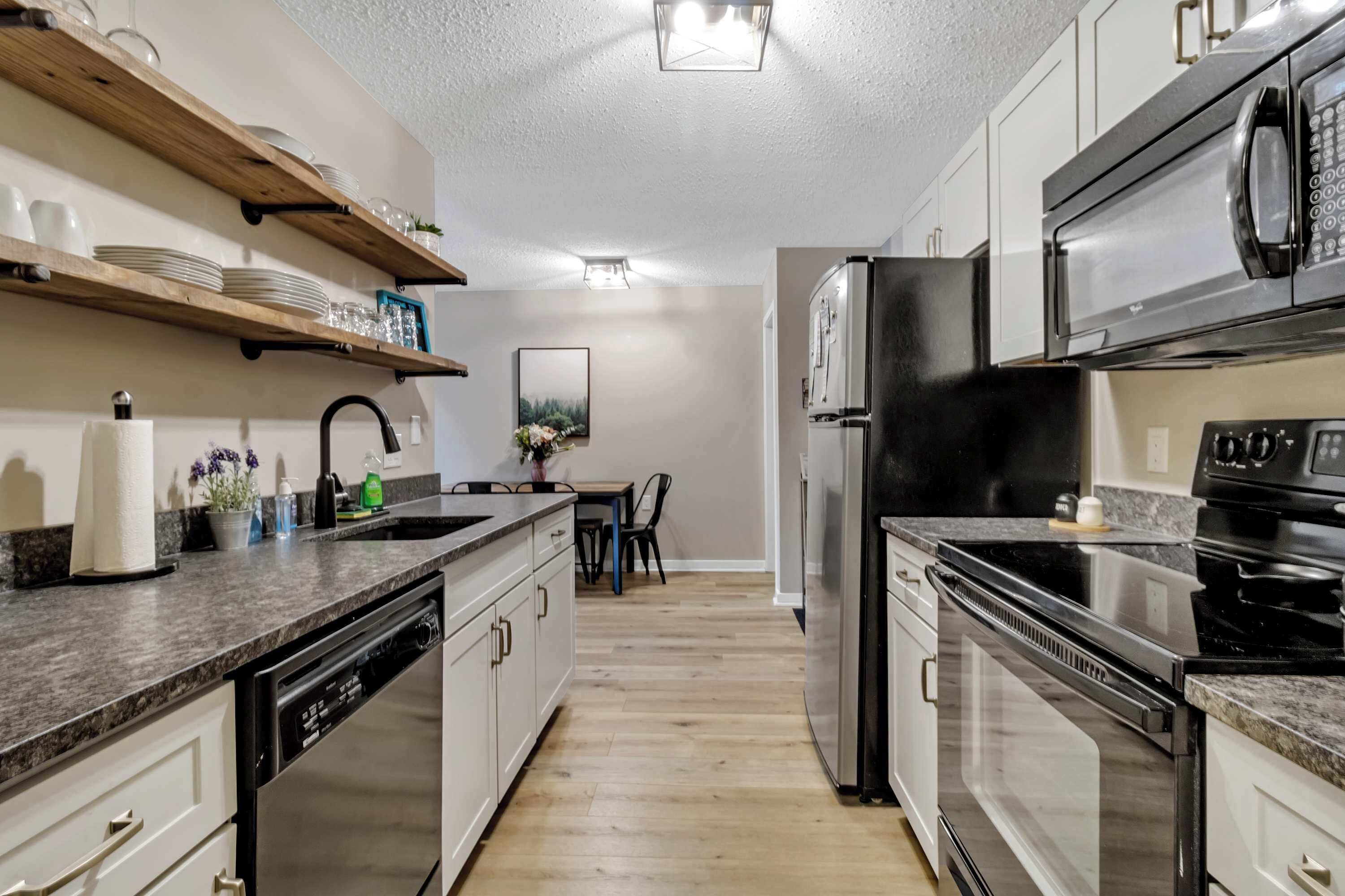 Une cuisine équipée d’appareils électroménagers intégrés, dotée d’étagères en bois et comprenant un coin repas avec des chaises.