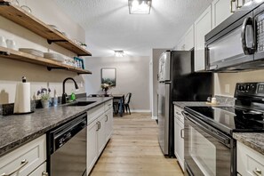 Una cocina con electrodomésticos integrados, estantes de madera y un comedor con sillas.