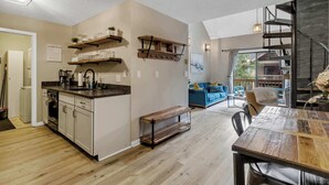 Cozinha moderna com prateleiras de madeira, uma mesa de jantar e uma escada que leva a um mezanino.