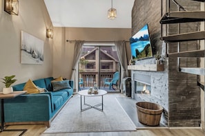 A living room with a sofa, a coffee table, a fireplace, and a TV mounted on the wall.