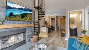 Uma sala de estar moderna com lareira, uma TV grande, uma escada e um espaço para refeições.