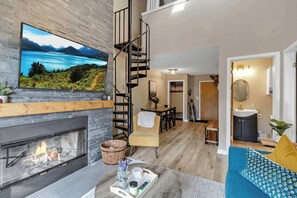 Una sala de estar moderna con chimenea, un televisor grande, una escalera y una zona de comedor.