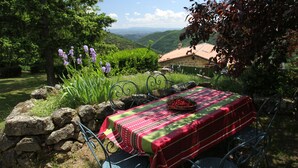 A dining table set outdoors with a view of hills and a house in the background. - DOMAINE DU VERNADEL GITE VERNADE  (Asperjoc)