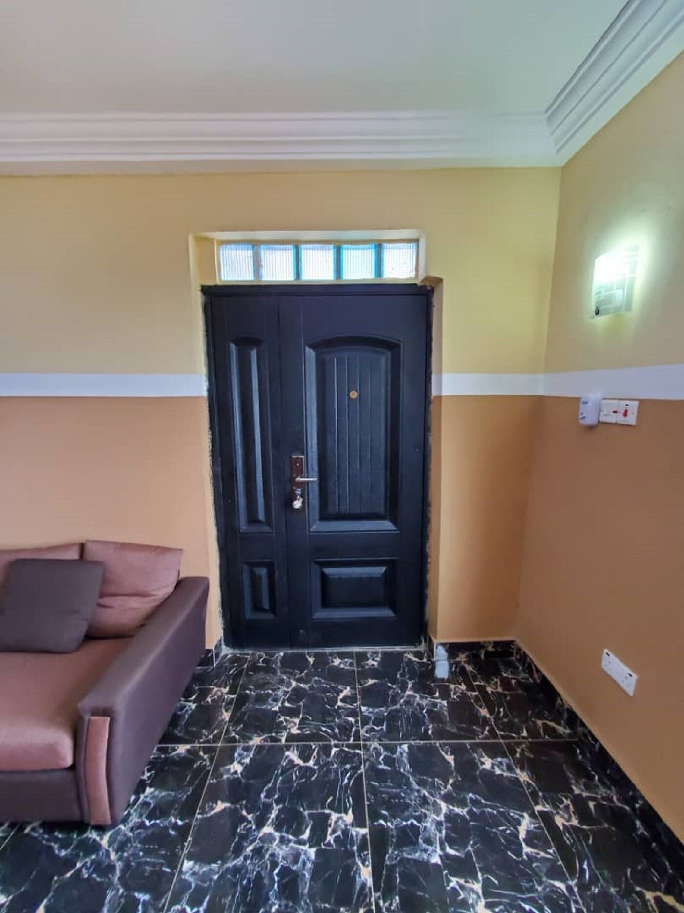 A room with a dark wooden door, a brown sofa, and a marble floor.