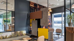 A modern interior with a sofa, chairs, a wooden reception desk, and a large window. - B&B HOTEL Bordeaux Bassins à flot (Bordeaux)