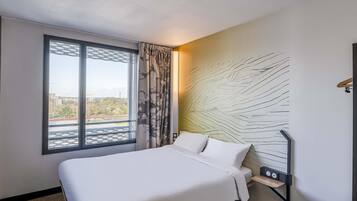A hotel room with a bed, a window with a view, a wall with a textured design, and a bedside table with a radio.