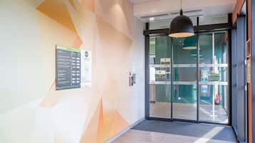 Un interior modern amb patrons geomètrics a la paret, una entrada amb porta de vidre i una lluminària penjant del sostre.