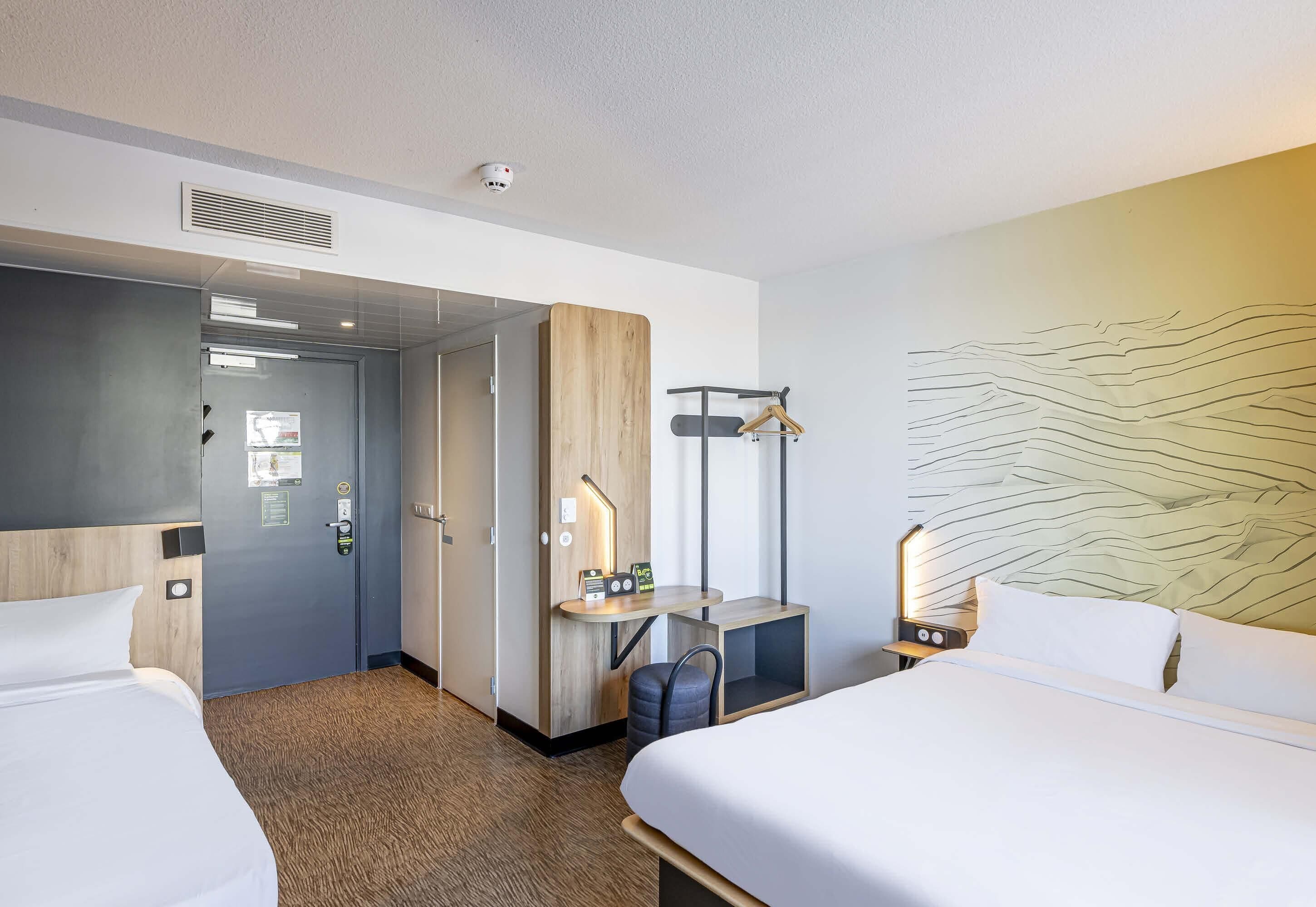 A hotel room with two beds, a desk, a chair, a coat rack, and a wall with a textured design.