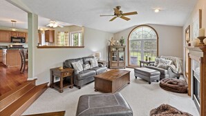 A spacious living room with a fireplace, leather furniture, and a large window providing a view of the outdoors. - Large Family Home in Heart of Brockport (Brockport)