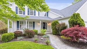 A two-story house with a front porch, a well-maintained garden, and a driveway leading to the entrance. - Large Family Home in Heart of Brockport (Brockport)