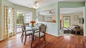 A dining area with a glass table and chairs, a ceiling fan, and a view of the outdoors through large windows. - Large Family Home in Heart of Brockport (Brockport)