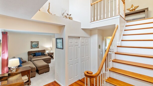 A spacious living area with a staircase leading to an upper floor, a cozy seating area with a sofa and ottoman, and a door with a mirror and picture frames. - Large Family Home in Heart of Brockport (Brockport)