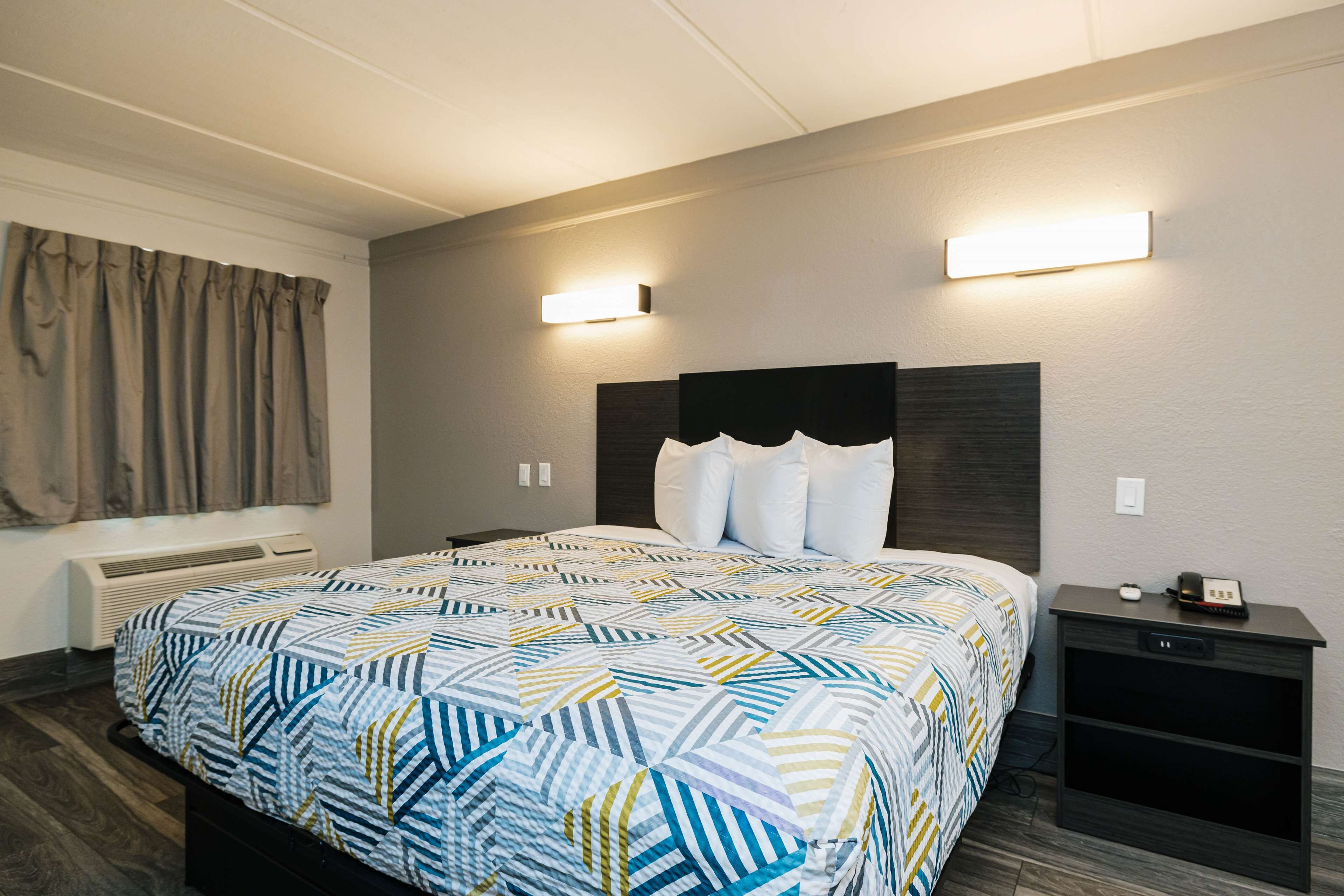 Ein Hotelzimmer mit einem großen Bett, zwei Nachttischen, einer Wandleuchte und einer Lampe am Bett.