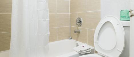 A bathroom with a bathtub, toilet, and shower curtain.