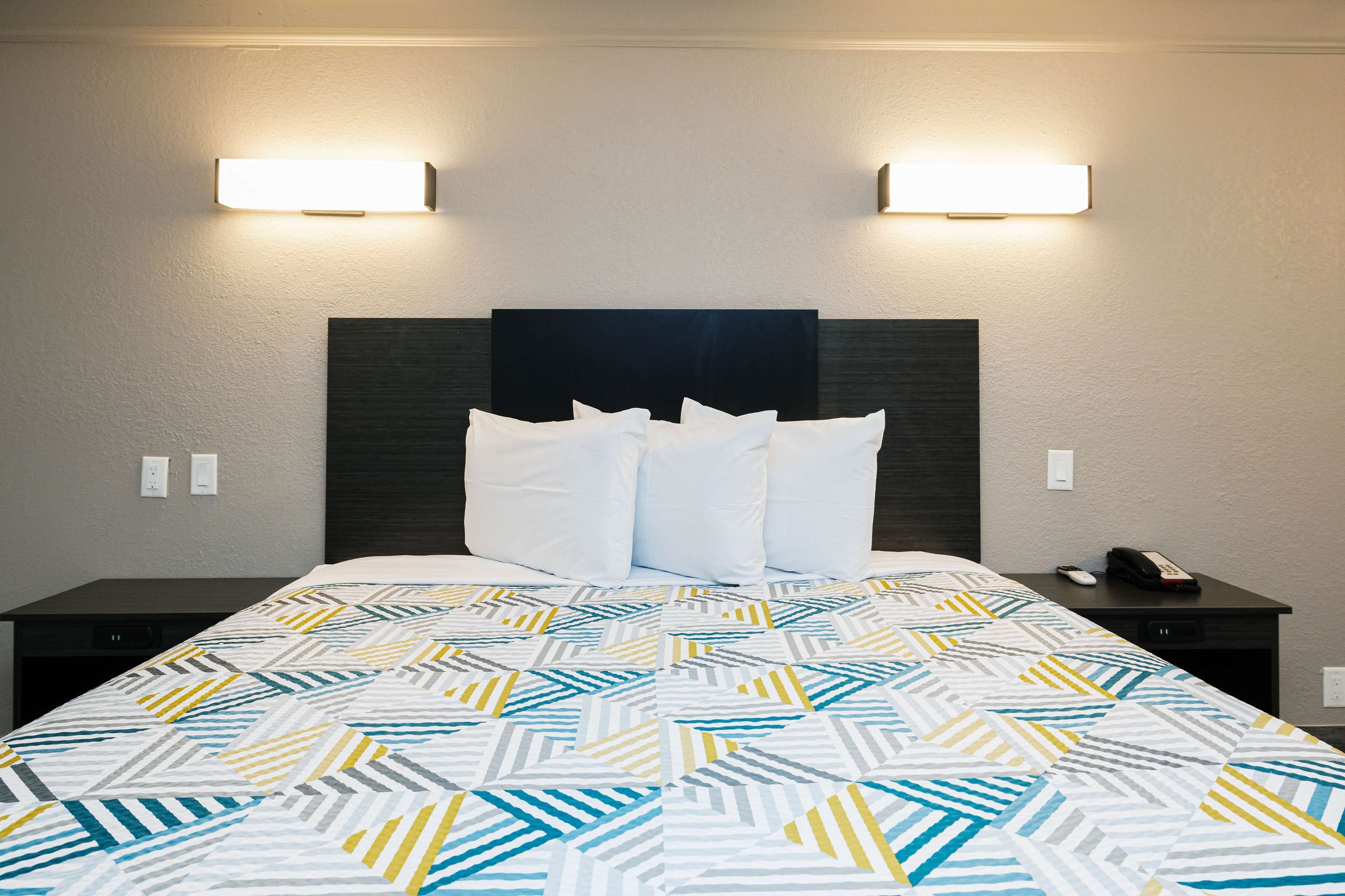 A hotel room with a bed, two bedside tables, a nightstand, and two wall-mounted lights.