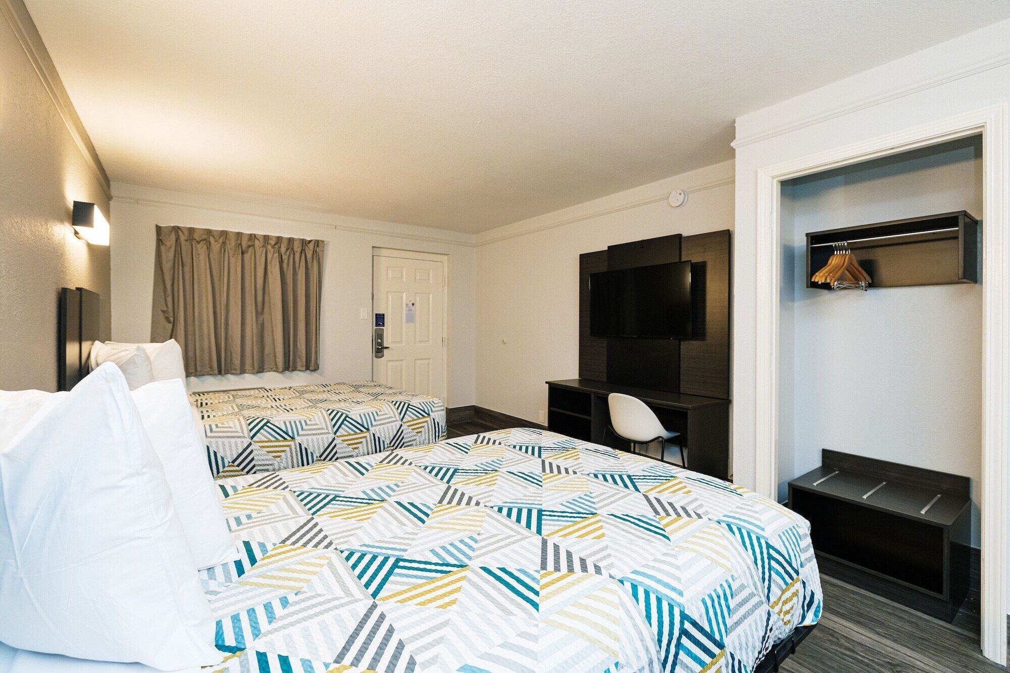 A hotel room with two beds, a desk, a chair, a television, and a coat rack.