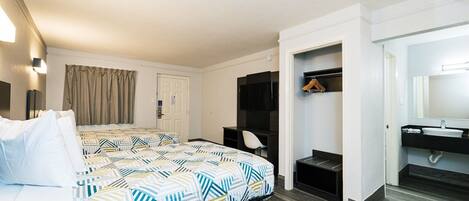 A hotel room with a large bed, a desk, a wardrobe, and a bathroom with a mirror and sink.