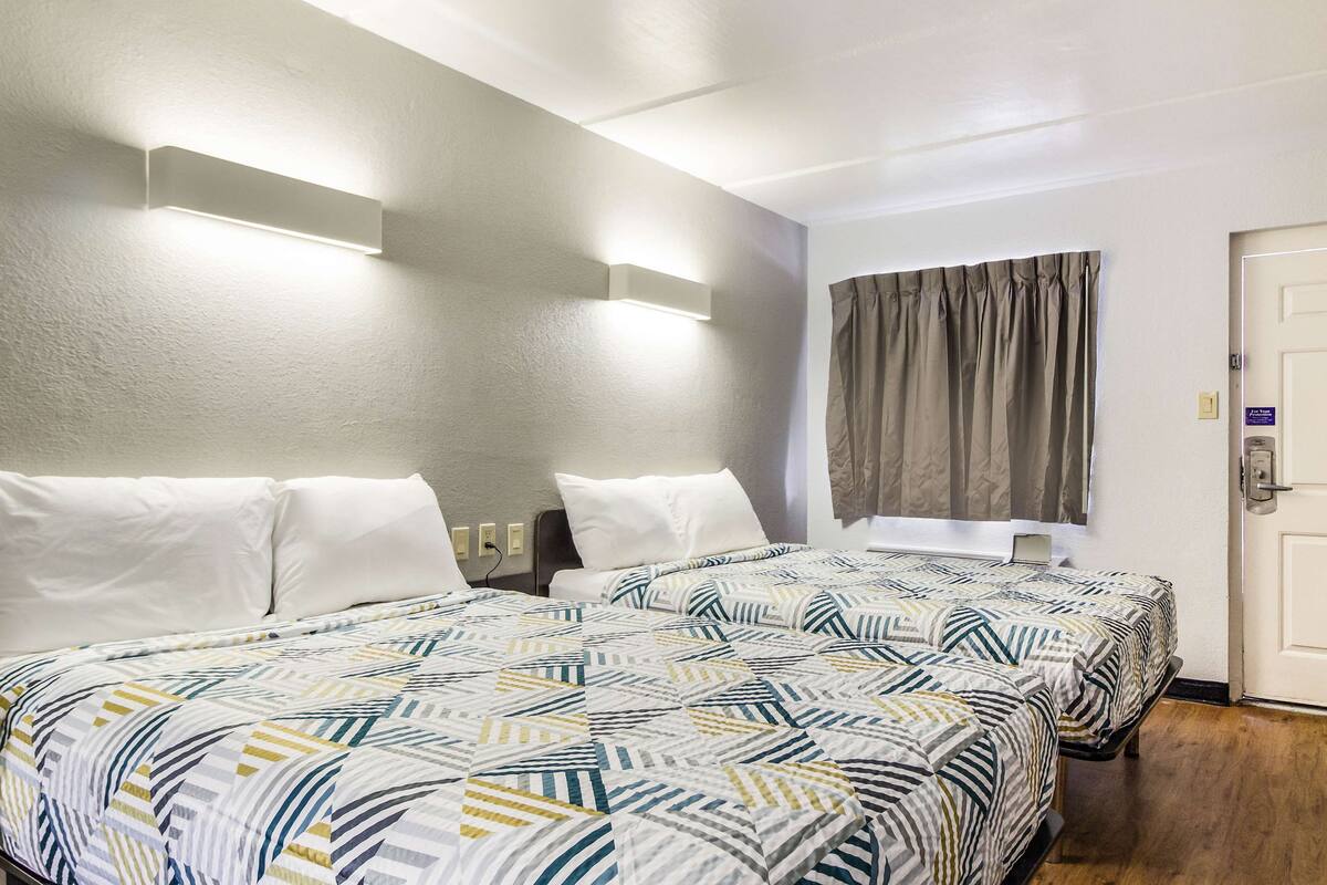 A hotel room with two beds, a large window with curtains, and a door with a lock.