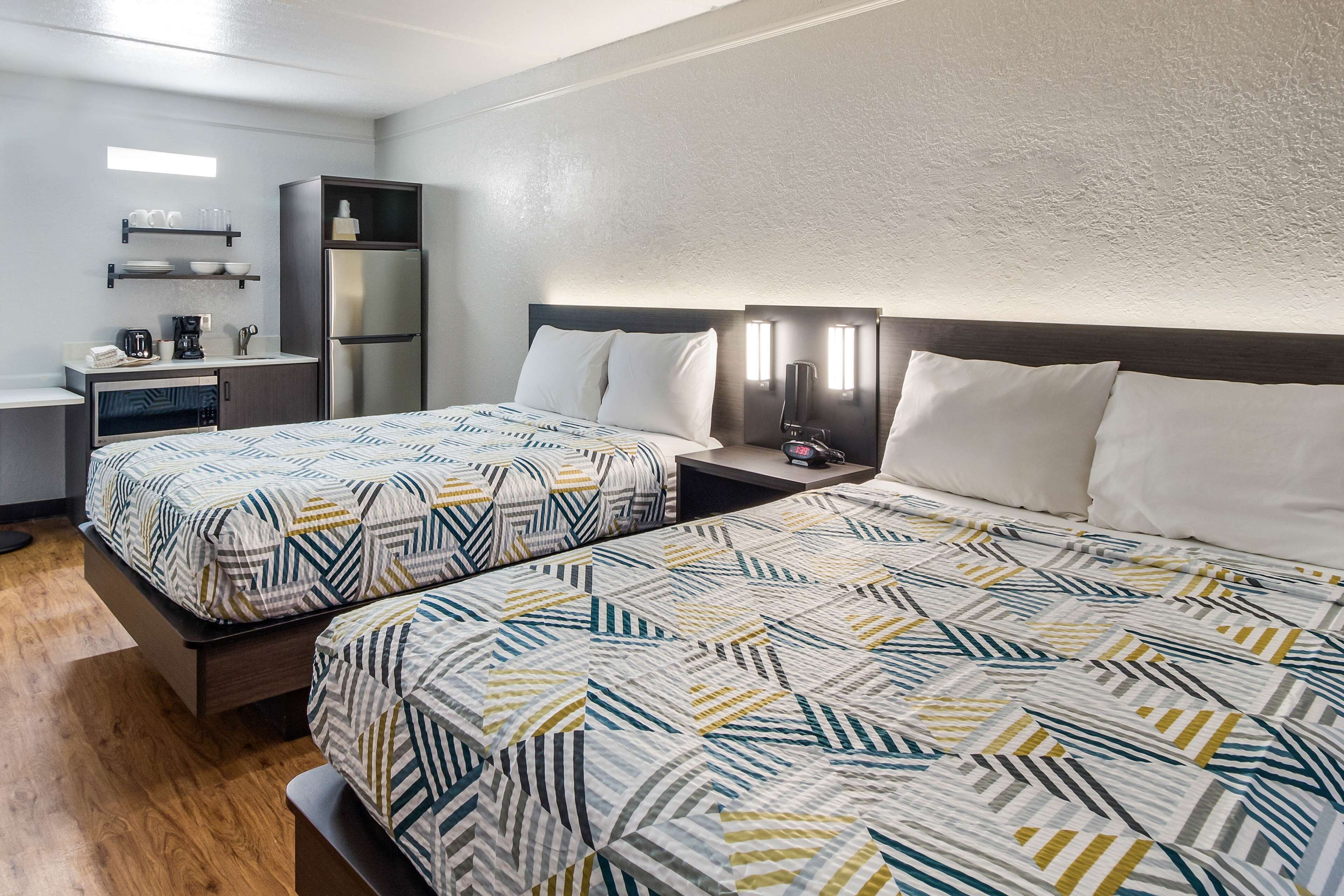 A hotel room with two beds, a kitchenette, and a small seating area.