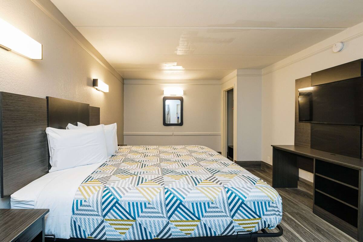 A hotel room with a bed, bedside tables, a TV, and a mirror.