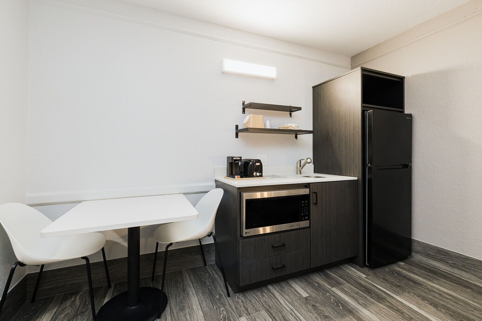 A compact kitchen with a white countertop, two white chairs, a black refrigerator, and a microwave.