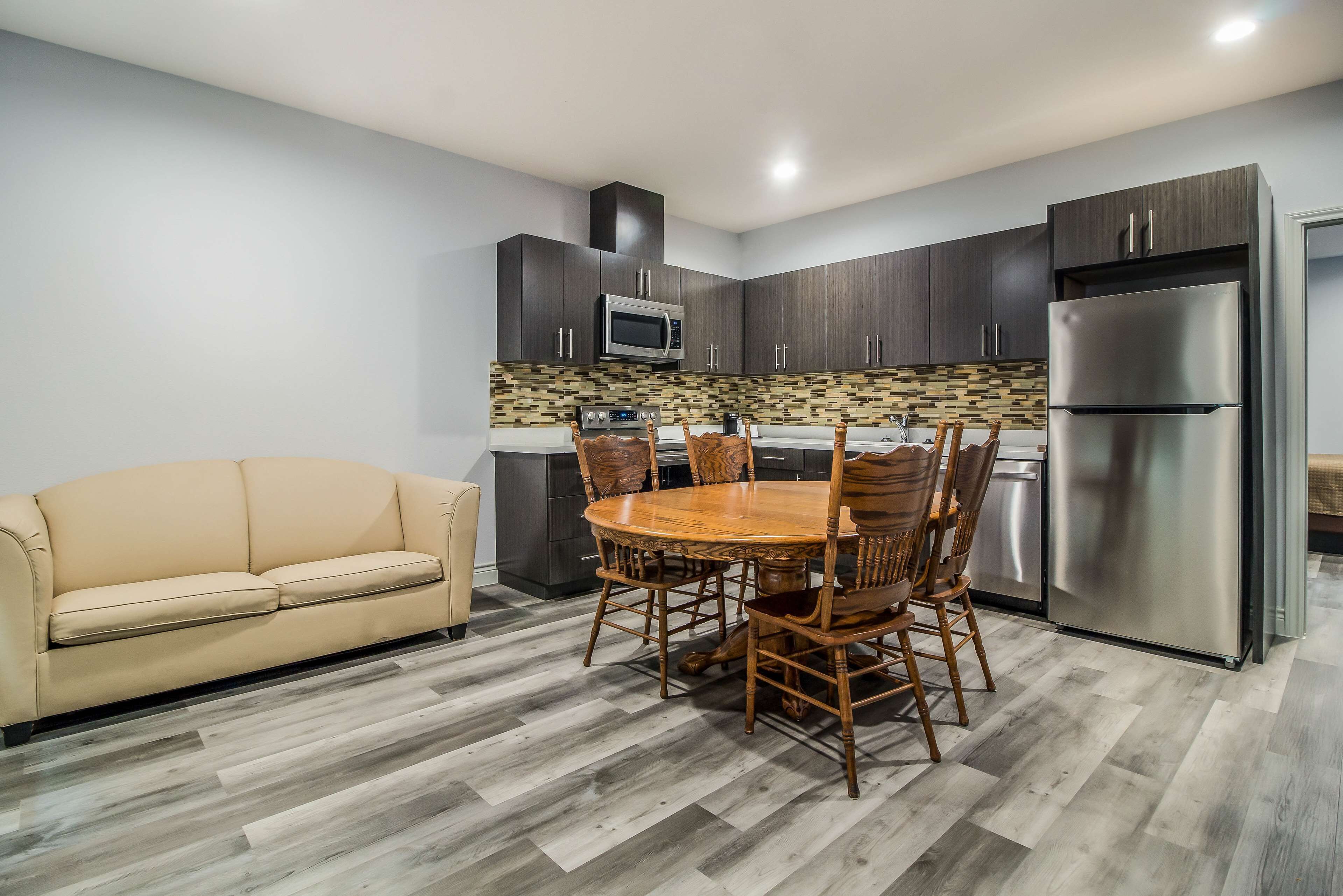 A modern kitchen with dark wood cabinets, a stainless steel refrigerator, and a wooden dining table with chairs.