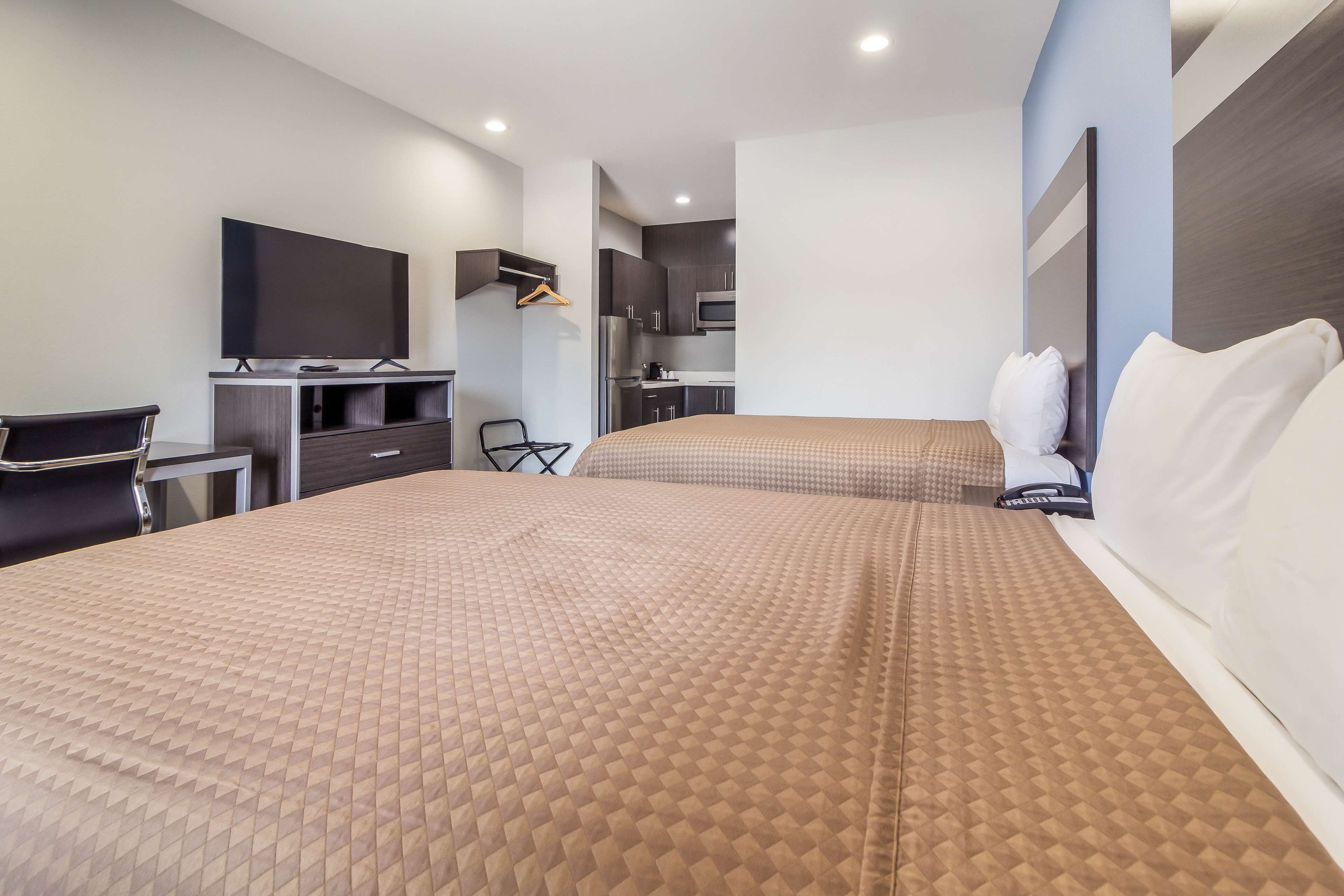 Quarto de hotel com duas camas, uma escrivaninha, televisão de tela plana, uma cadeira e uma cozinha compacta.