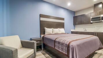 Una habitación de hotel moderna con una cama, una silla, una mesita de noche, un microondas y un lavamanos.