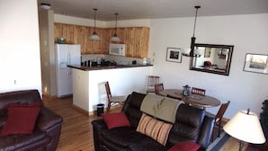 Ein Wohnzimmer mit Ledersofa, einem Esstisch mit Stühlen und einer Küchenzeile mit Holzschränken und einem Kühlschrank.