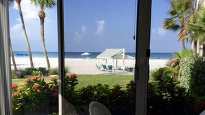 A patio with a view of the beach, including palm trees and a white building with a roof. - Island House Beach Resort 2N (Siesta Key)