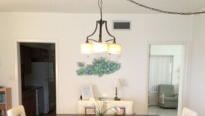 A dining area with a dark wooden table, white upholstered chairs, a chandelier, and a decorative wall piece. - Island House Beach Resort 2N (Siesta Key)