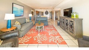 Un salón con sofá, mesa de centro y alfombra roja estampada. Hay un televisor y un mueble con un objeto decorativo encima.