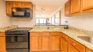 Una cocina con armarios de madera, encimera de granito, estufa negra, microondas y licuadora.