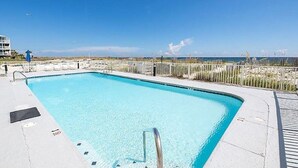 Una piscina rectangular con agua cristalina azul, rodeada por un patio de concreto y una cerca de madera.