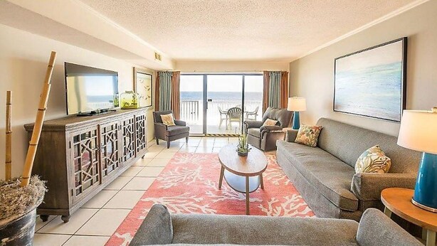 Un salón amplio con sofá, sillones, una mesa de centro y televisor. Cuenta con un balcón con vistas al océano.